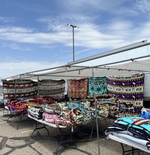 Colorful blankets displayed at a market under a canopy, with a blue sky in the background.