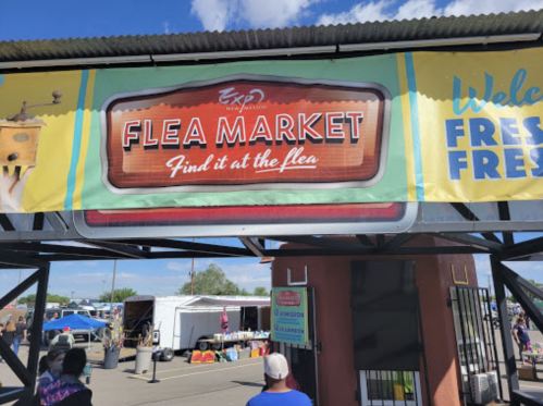 A colorful sign for a flea market reads "Find it at the flea" with people gathered below.