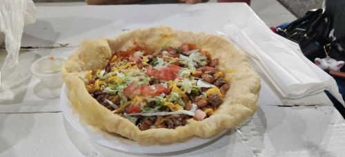 A colorful taco salad in a crispy shell, filled with beef, beans, cheese, lettuce, tomatoes, and salsa on a table.