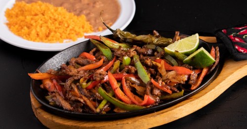 plate of fajita vegetables and peppers in a skillet next to a plate of rice and beans