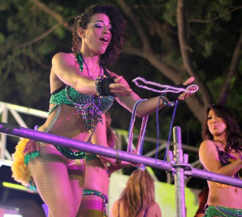 A performer in a colorful costume dances on stage, holding beads, with another dancer beside her.
