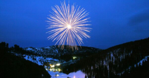A bright firework explodes in the night sky over a snowy mountain landscape.