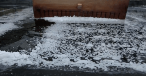A wooden tool rests on a surface covered with scattered salt crystals and ice, creating a textured, frosty scene.