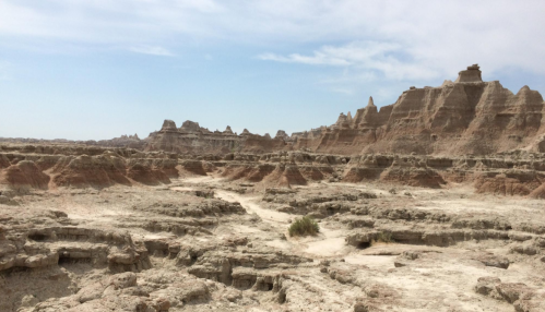 A rugged, dry landscape with layered rock formations and a clear sky, showcasing the beauty of a desert terrain.