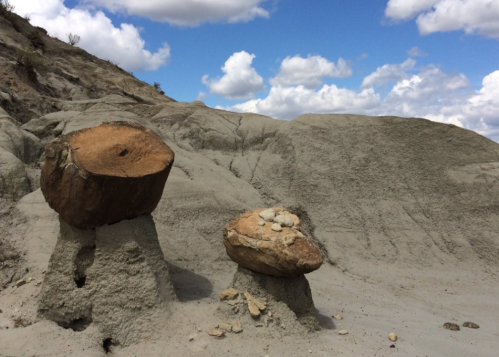 Two large, weathered rock formations on a sandy landscape under a partly cloudy sky.