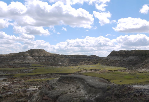 A vast landscape with rolling hills, green patches, and a blue sky dotted with fluffy clouds.