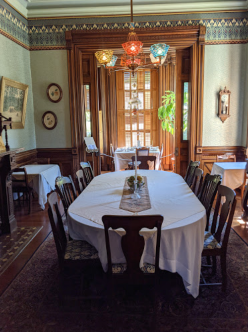 A dining room with a large table set for a meal, surrounded by wooden chairs and decorative light fixtures.