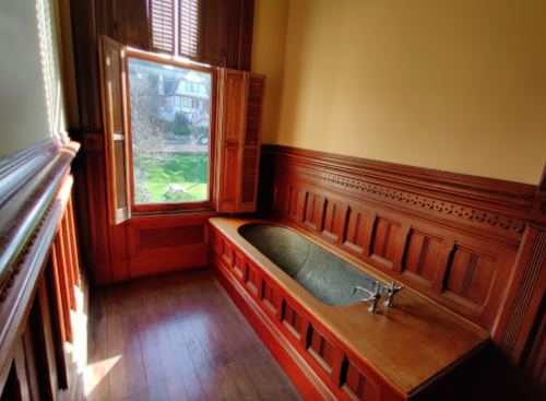 A vintage bathroom with a stone bathtub, wooden paneling, and a window overlooking a garden.