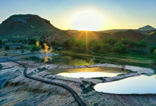 A serene landscape at sunrise, featuring hot springs, reflections in water, and rolling hills in the background.
