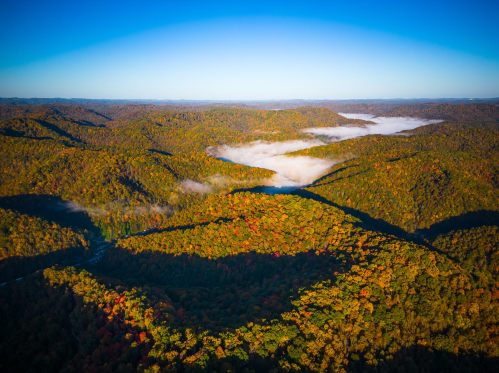Aerial view of colorful autumn hills with mist in the valleys under a clear blue sky.
