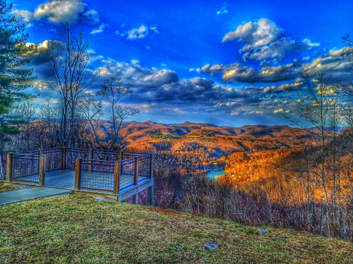 Scenic overlook with a view of rolling hills, a lake, and a vibrant sky filled with clouds.