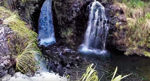 A scenic view of two waterfalls cascading into a rocky pool, surrounded by lush greenery.
