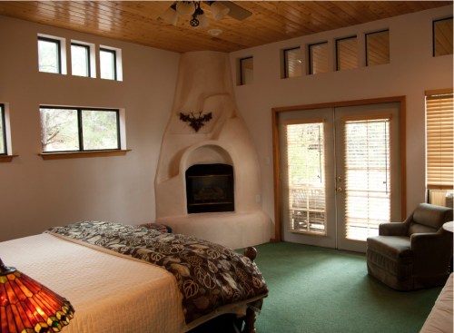 Cozy bedroom with a fireplace, large windows, and a green carpet, featuring a bed and a comfortable chair.