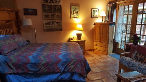 Cozy bedroom with a patterned bedspread, wooden furniture, warm lighting, and a door leading to an outdoor area.
