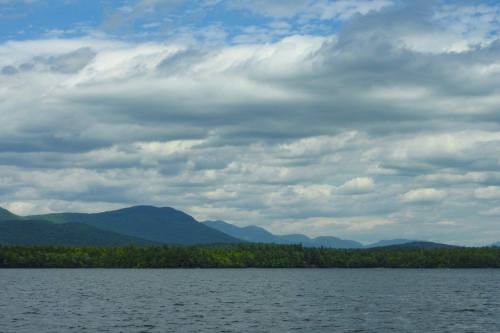 A serene lake surrounded by lush green mountains under a cloudy sky.