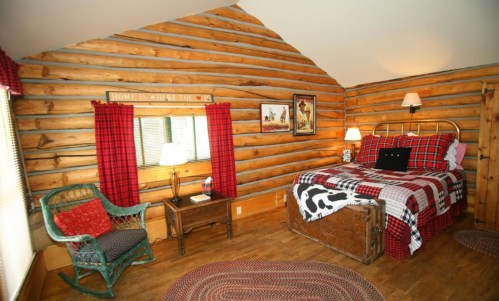 Cozy log cabin bedroom with a plaid bedspread, wooden accents, and a rustic chair by the window.