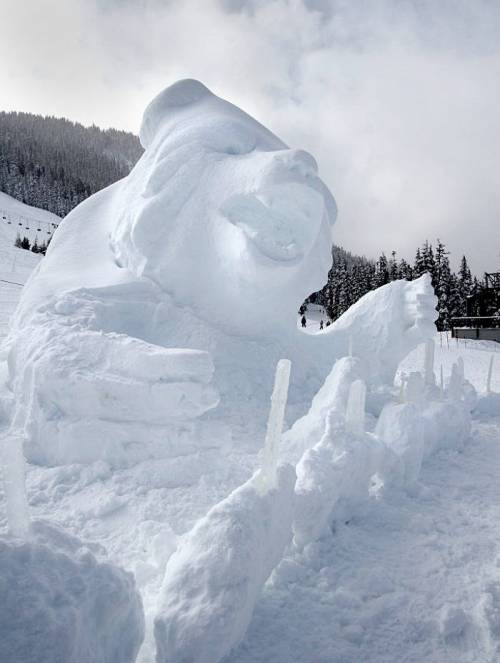 A large snow sculpture of a bear with a playful expression, surrounded by icicles and a snowy landscape.