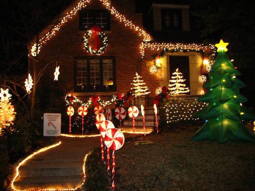 A festive house decorated with Christmas lights, candy cane decorations, and an inflatable Christmas tree.