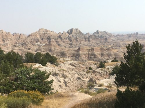 A vast landscape of rugged rock formations and sparse vegetation under a hazy sky, showcasing natural erosion patterns.