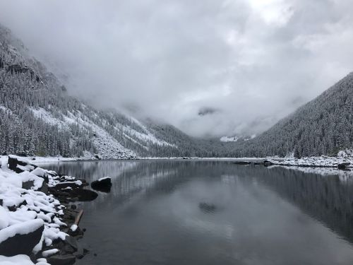 A serene winter landscape featuring a snow-covered lake surrounded by mountains and cloudy skies.