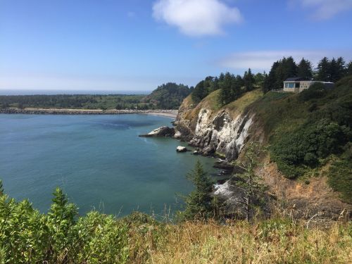 A scenic coastal view featuring cliffs, lush greenery, and calm blue waters under a clear sky.