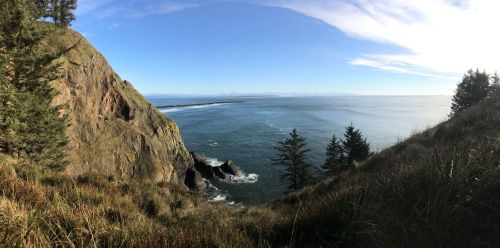 Panoramic view of a coastal landscape with cliffs, ocean waves, and a clear blue sky.