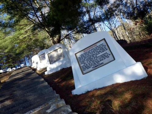 Gravestones lined along a path in a wooded area, featuring inscriptions on white stone markers.