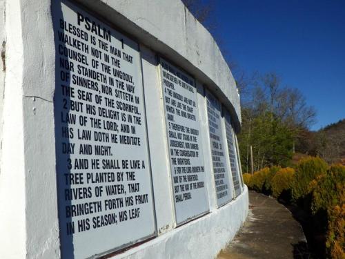 A stone wall displays the text of Psalm 1, surrounded by greenery and a clear blue sky.