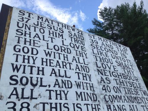 A large billboard displaying biblical verses from St. Matthew, with bold black text against a white background.