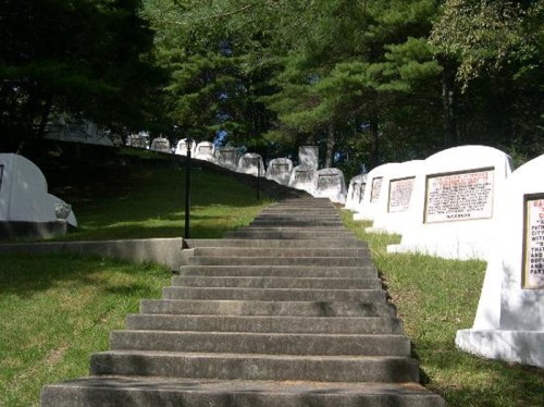 A stone staircase leads up a grassy hill lined with white tombstones and memorial plaques under a tree canopy.