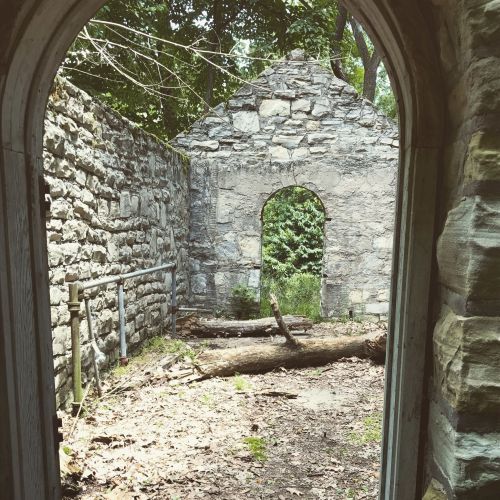 View through an archway into a stone ruin surrounded by trees and overgrown vegetation.
