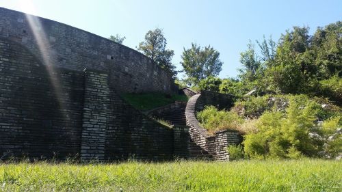A winding stone path leads up a grassy hill, surrounded by trees and a circular stone wall in the background.
