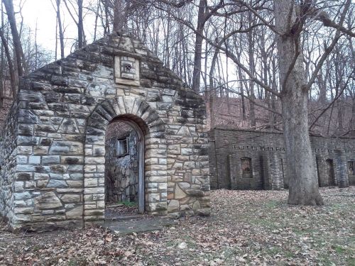 Stone structures nestled in a wooded area, surrounded by bare trees and fallen leaves.