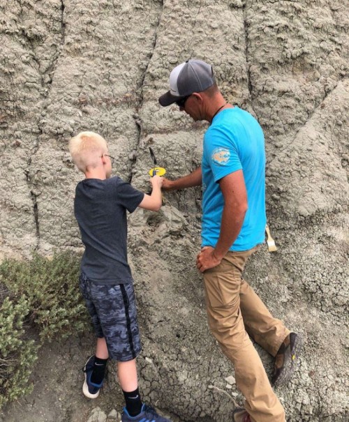 A man and a boy examine a rock formation, using tools to explore the geological features.