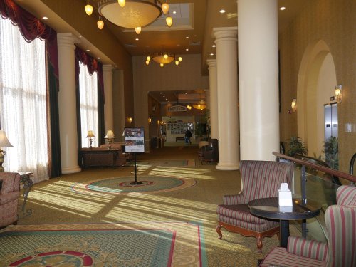 Brightly lit hotel lobby with tall windows, elegant decor, and seating areas featuring striped chairs and decorative pillars.