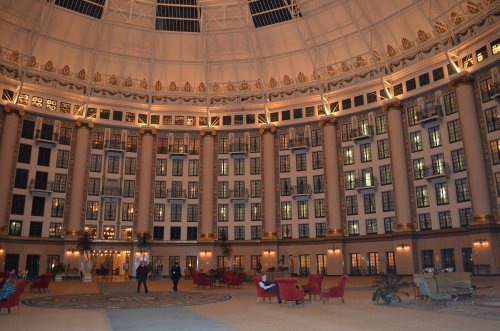 A spacious, elegantly designed lobby with tall columns, large windows, and cozy seating areas, illuminated warmly.