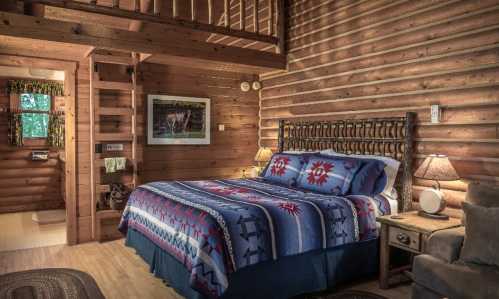 Cozy log cabin interior featuring a bed with a colorful blanket, wooden walls, and a lofted sleeping area.