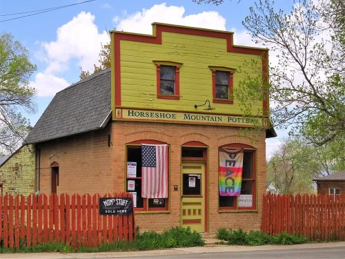 Colorful pottery shop with a green and yellow exterior, featuring flags and a wooden fence.