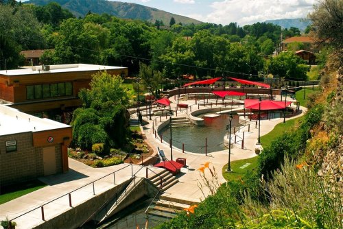A scenic view of a landscaped area with a circular pool, surrounded by greenery and shaded seating under red canopies.