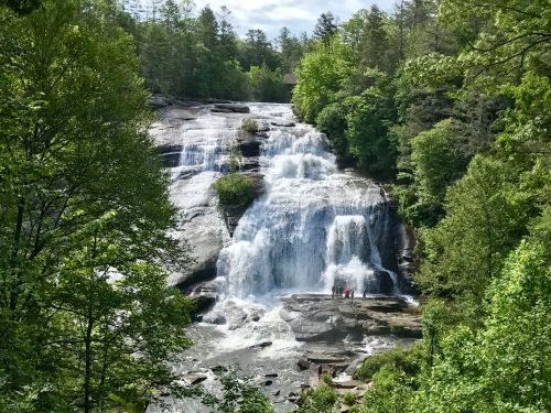 A scenic waterfall cascades down rocky cliffs, surrounded by lush green trees and a clear blue sky.