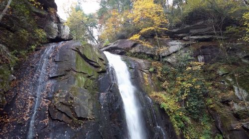 A cascading waterfall flows down rocky cliffs, surrounded by autumn foliage and lush greenery.
