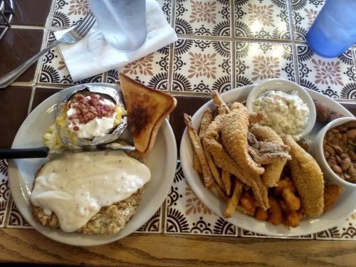 A plate of fried catfish, hushpuppies, and coleslaw, alongside a baked potato with toppings and toast.