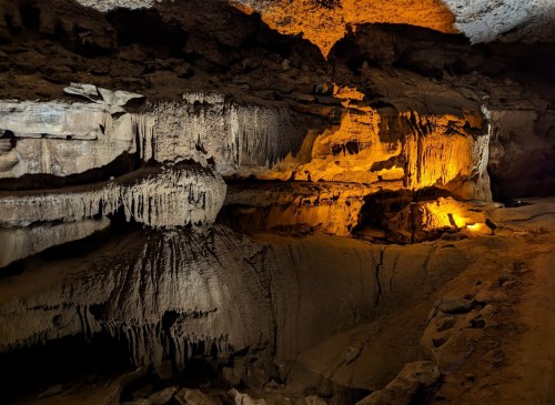 Stalactites and stalagmites in a dimly lit cave, with warm lighting highlighting the rock formations.