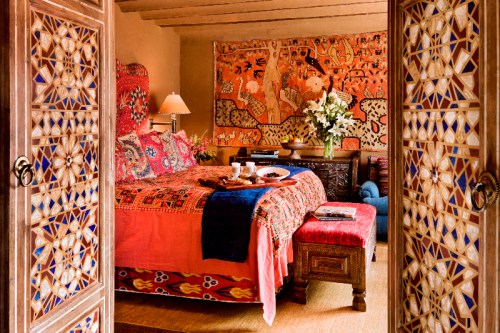 A cozy bedroom with vibrant textiles, a wooden bed, and decorative walls, creating a warm and inviting atmosphere.