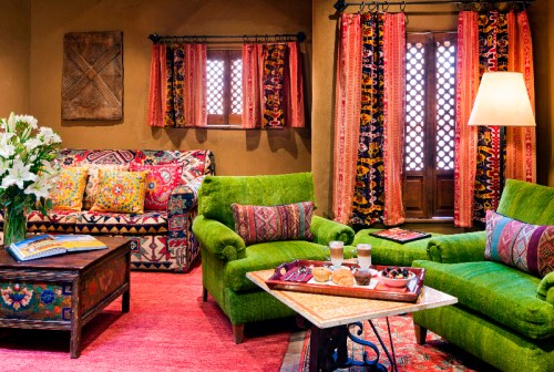 Cozy living room with vibrant green furniture, colorful textiles, and a wooden coffee table with snacks and drinks.