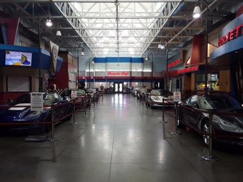 Interior of a car museum featuring several classic Corvettes lined up with barriers and signage. Bright, spacious setting.