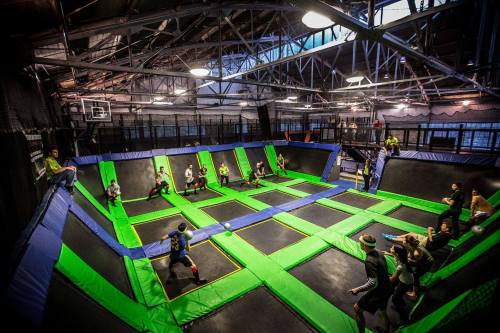 A vibrant indoor trampoline park with multiple trampolines and people playing and jumping around.