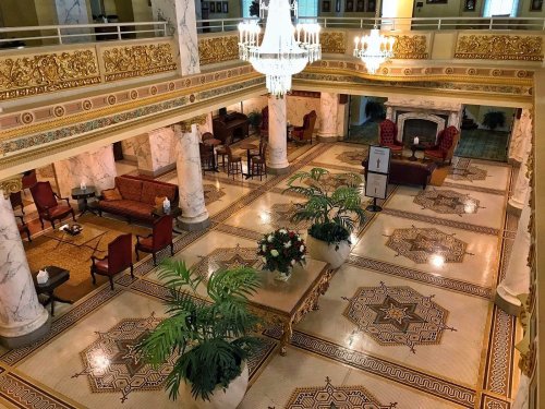 Elegant hotel lobby featuring marble floors, ornate decor, chandeliers, and plush seating areas.