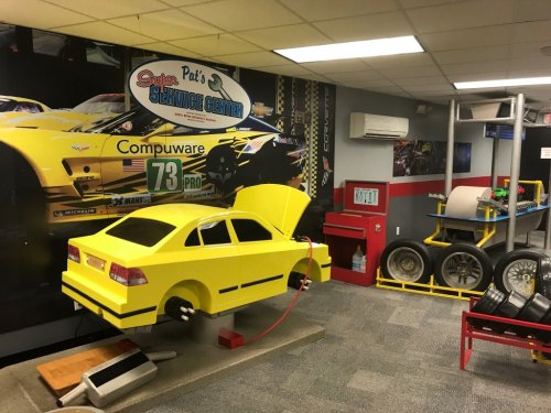 A bright yellow toy car in a garage-themed room with racing posters and equipment in the background.