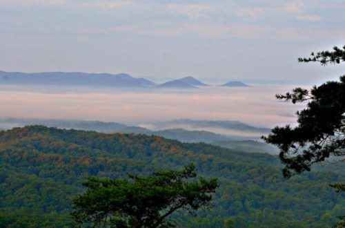 A misty mountain landscape with rolling hills and distant peaks under a cloudy sky.